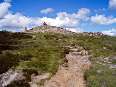 The prehistoric cairn in the centre with the trig point on its left and a modern cairn on its right