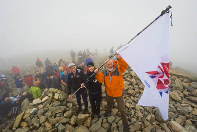 Sir Chris raises the Olympic flag, with Jos Naylor and Laura Park, on the summit of Scafell Pike