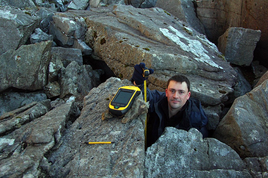 Aled Williams measures the drop from the GPS unit to the ground among the boulders on the col. Photo: Myrddyn Phillips