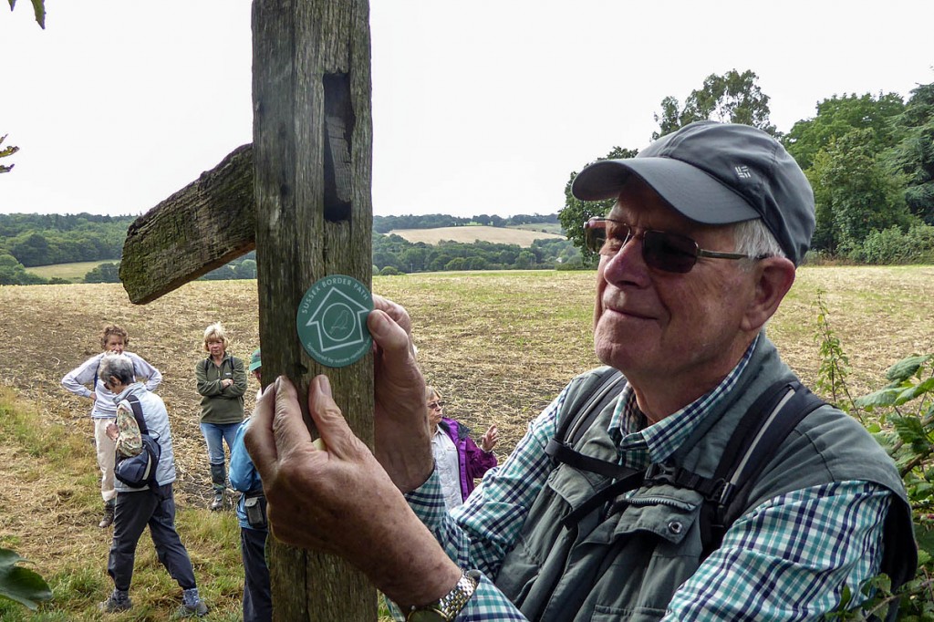Ramblers volunteer Jerry Kind fixes a label to a roadside finger post on the Sussex Border Path