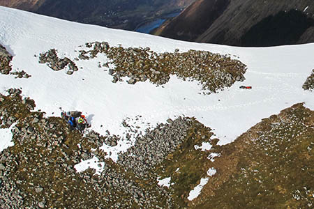 A close up of the rescue scene, with the Royal Navy winchman treating the walker on the lower edge of the snow A close up of the rescue scene, with the Royal Navy winchman treating the walker on the lower edge of the snow