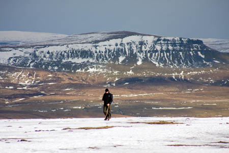 A walker on Ingleborough's frozen summit, with Pen-y-ghent in the distance