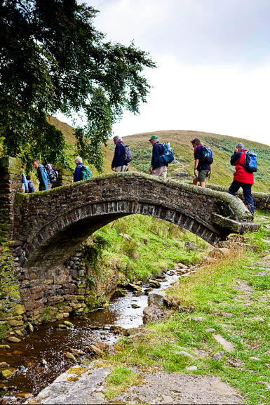 Walkers on a packhorse bridge in the South Pennines