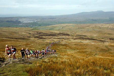 Three Peaks Race runners ascend Pen-y-ghent, with Ingleborough in the distance Three Peaks Race runners ascend Pen-y-ghent, with Ingleborough in the distance