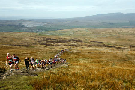 Three Peaks Race runners ascend Pen-y-ghent, with Ingleborough in the distance